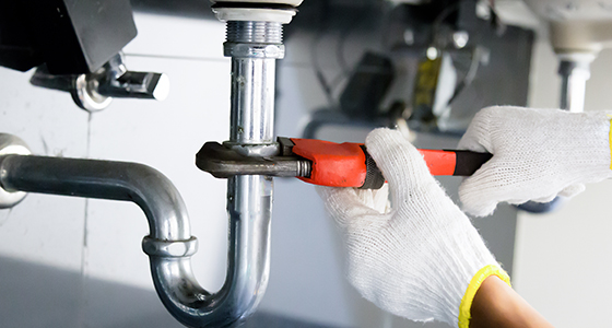 a plumber wearing white cotton gloves using a wrench to tighten up a u-bend pipe